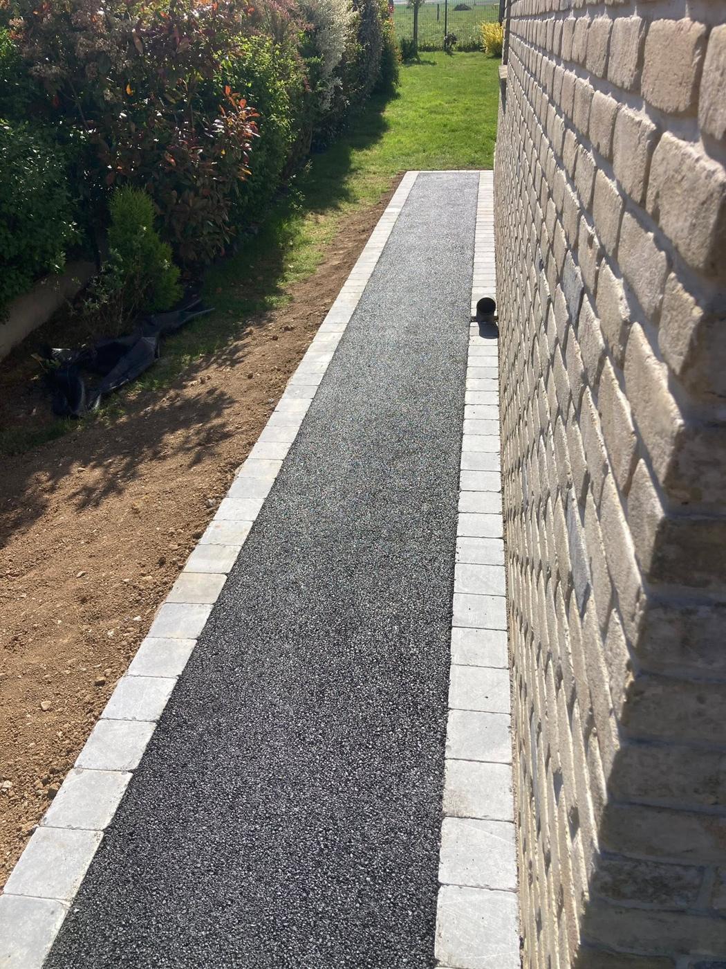 Allée en enrobé entre une frise en pierre bleue et un mur